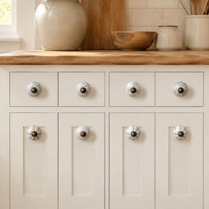 May include: A set of off-white kitchen cabinets featuring eight round ceramic knobs with various grey and white patterns. Each knob is centred on a drawer or cabinet door and includes a dark metallic centre screw and a small circular base.