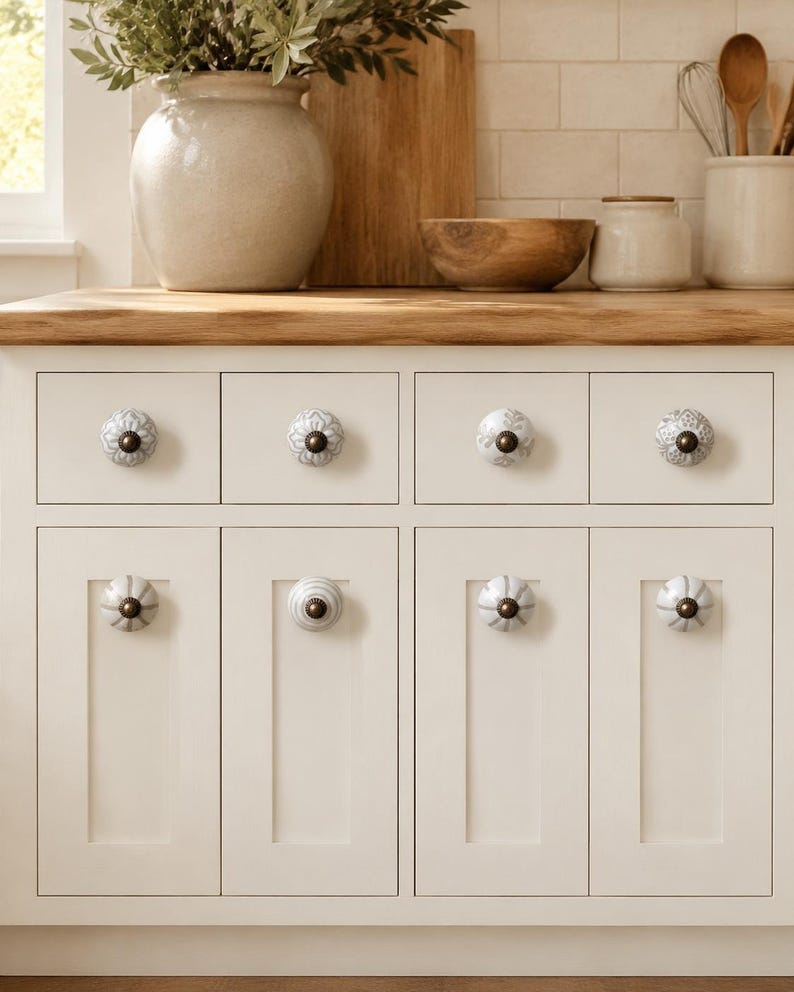 May include: A set of off-white kitchen cabinets featuring eight round ceramic knobs with various grey and white patterns. Each knob is centred on a drawer or cabinet door and includes a dark metallic centre screw and a small circular base.