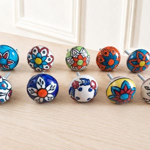 May include: A collection of ten round ceramic cabinet knobs, each featuring unique hand-painted floral patterns in vibrant colors including blue, red, orange, green, yellow, and white. Each knob includes a silver-toned metal screw for installation.
