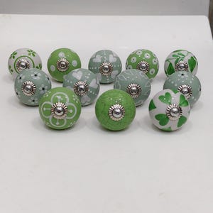 Pode incluir: Uma cole&ccedil;&atilde;o de puxadores decorativos de cer&acirc;mica em tons de verde e branco. Os puxadores apresentam padr&otilde;es florais, de cora&ccedil;&atilde;o e de pontos com ferragens met&aacute;licas prateadas. Adequados para arm&aacute;rios e gavetas.