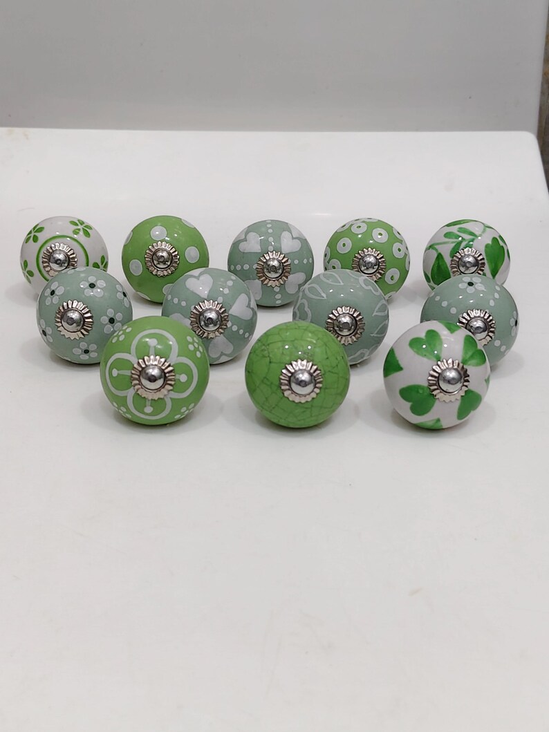 Pode incluir: Uma cole&ccedil;&atilde;o de puxadores decorativos de cer&acirc;mica em tons de verde e branco. Os puxadores apresentam padr&otilde;es florais, de cora&ccedil;&atilde;o e de pontos com ferragens met&aacute;licas prateadas. Adequados para arm&aacute;rios e gavetas.