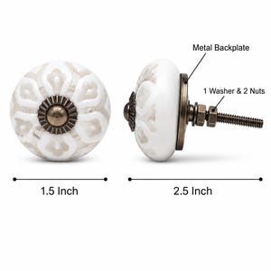 May include: A round white ceramic knob with a light grey floral pattern and an antique bronze metal centre. The knob has a diameter of 3.81 cm and a length of 6.35 cm, including a metal backplate, one washer, and two nuts on the threaded bolt.