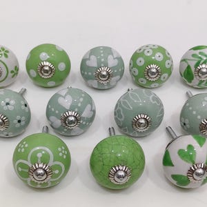 Pode incluir: Uma cole&ccedil;&atilde;o de puxadores de arm&aacute;rio decorativos em cer&acirc;mica em v&aacute;rios tons de verde e branco. Os puxadores apresentam padr&otilde;es florais, de cora&ccedil;&atilde;o e de bolinhas, com ferragens met&aacute;licas prateadas.