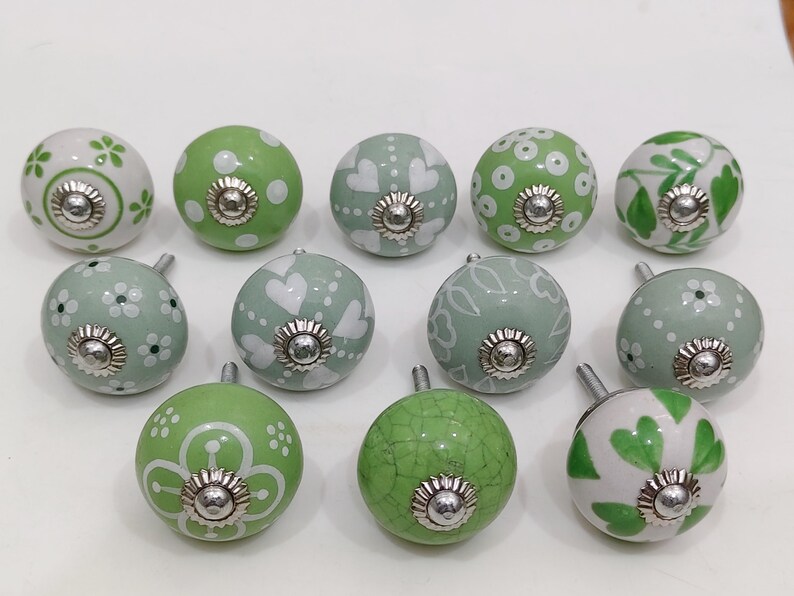 Pode incluir: Uma cole&ccedil;&atilde;o de puxadores de arm&aacute;rio decorativos em cer&acirc;mica em v&aacute;rios tons de verde e branco. Os puxadores apresentam padr&otilde;es florais, de cora&ccedil;&atilde;o e de bolinhas, com ferragens met&aacute;licas prateadas.