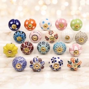 May include: A collection of seventeen round ceramic cabinet knobs featuring various patterns including polka dots, floral motifs, and crackled glazes. Each knob is finished with a central gold-toned metal hardware piece for mounting.