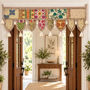 May include: A decorative fabric door valance featuring a patchwork of colorful embroidered panels with floral and geometric patterns. The valance has a scalloped bottom edge finished with cream-colored tassels hanging from each point and corner.