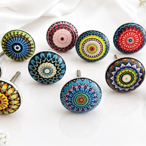 May include: A collection of nine round cabinet knobs featuring intricate, colorful mandala-style patterns in shades of red, blue, yellow, green, and pink. Each knob has a smooth, glossy surface and a metal screw attachment extending from the back.