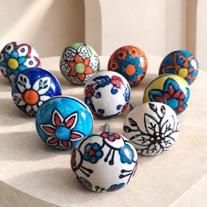 Peut inclure: Une collection de dix boutons de placard ronds en céramique présentant divers motifs floraux peints à la main dans des couleurs vives, notamment bleu, rouge, orange, jaune, vert et noir sur fond blanc ou coloré, chacun avec une vis de fixation.