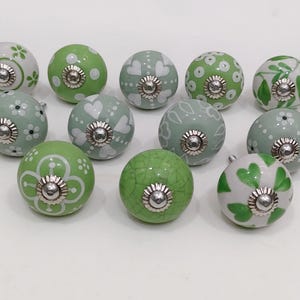 Pode incluir: Uma cole&ccedil;&atilde;o de puxadores de arm&aacute;rio decorativos em cer&acirc;mica em v&aacute;rios tons de verde e branco. Os puxadores apresentam padr&otilde;es florais, de cora&ccedil;&atilde;o e de pontos, com ferragens met&aacute;licas prateadas.