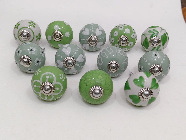 Pode incluir: Uma cole&ccedil;&atilde;o de puxadores de arm&aacute;rio decorativos em cer&acirc;mica em v&aacute;rios tons de verde e branco. Os puxadores apresentam padr&otilde;es florais, de cora&ccedil;&atilde;o e de pontos, com ferragens met&aacute;licas prateadas.