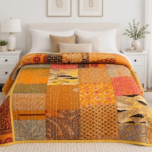 Könnte beinhalten: Eine Patchwork-Tagesdecke mit einer Vielzahl rechteckiger Stoffbahnen in Orange-, Gelb-, Gold- und Brauntönen. Die Decke zeigt verschiedene Muster, darunter florale, geometrische und abstrakte Drucke, die durch sichtbare weiße Steppstiche verbunden sind.