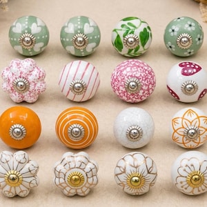 Può includere: Una collezione di pomelli decorativi in ceramica in vari colori e motivi. I disegni includono motivi floreali, a righe e a pois. Ogni pomello ha una base argentata. Adatto per mobili o decorazioni per la casa.