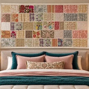 Op de afbeelding: Een grote rechthoekige wandhanger met een patchworkontwerp van diverse stoffen vierkanten in tinten rood, goud, groen en grijs. Het textiel toont uiteenlopende bloem- en geometrische patronen, omlijst door een eenvoudige witte rand.