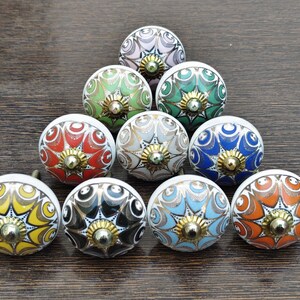 Pu&ograve; includere: Una collezione di dieci pomelli rotondi in ceramica per mobili disposti a triangolo. Ogni pomello presenta un motivo floreale multicolore unico con linee intricate e un elemento centrale in metallo dorato all'apice della cupola.