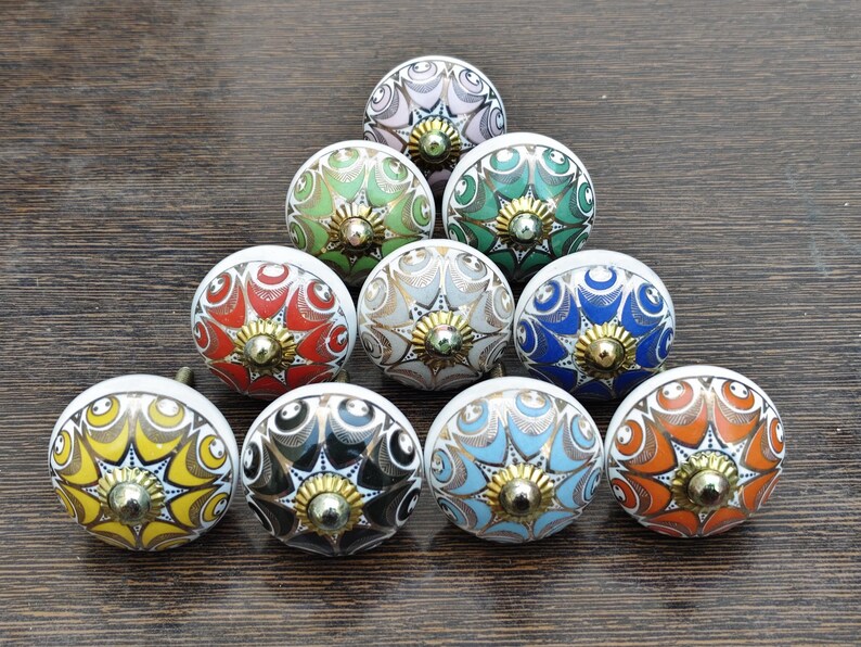 Pu&ograve; includere: Una collezione di dieci pomelli rotondi in ceramica per mobili disposti a triangolo. Ogni pomello presenta un motivo floreale multicolore unico con linee intricate e un elemento centrale in metallo dorato all'apice della cupola.