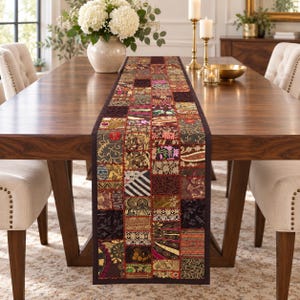 May include: A rectangular table runner featuring a patchwork design of various fabric squares in shades of deep red, gold, black, and brown. The runner displays intricate embroidery, metallic thread accents, and diverse floral and geometric patterns.