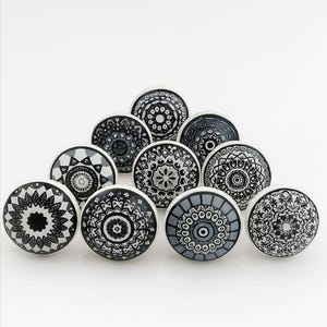 May include: A collection of decorative cabinet knobs with intricate black and white mandala designs. The knobs are round with a white base and feature various geometric patterns. These knobs are perfect for adding a touch of bohemian style to furniture.