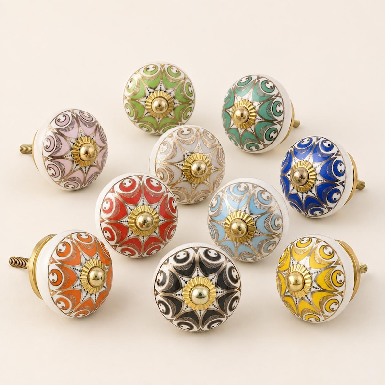 Pu&ograve; includere: Una collezione di nove pomelli rotondi in ceramica per mobili, ognuno caratterizzato da un motivo floreale multicolore unico con accenti dorati e un tappo centrale in metallo dorato. I pomelli sono disposti in gruppo, mostrando colori tra cui rosso, blu, verde, giallo, arancione, rosa, nero e bianco.