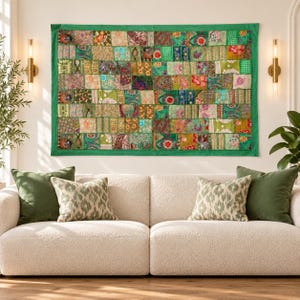 Könnte beinhalten: Ein rechteckiger Wandbehang mit einem Patchwork-Design aus verschiedenen grünen, goldenen und bunten Stoffquadraten. Das Textil ist von einem einfarbigen grünen Rahmen umgeben und zeigt eine Vielzahl komplizierter Blumen- und Geometriemuster.