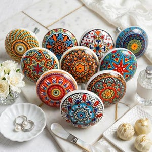 May include: A collection of ten round ceramic cabinet knobs featuring vibrant, multi-colored geometric and floral patterns in shades of orange, blue, red, green, and yellow. Each knob displays a unique, intricate design on its circular face.