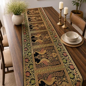Pode incluir: Um caminho de mesa decorativo com um design intrincado com pássaros dourados e vermelhos sobre um fundo preto. O caminho de mesa é colocado sobre uma mesa de madeira escura, junto com velas, uma tigela e um vaso de flores. As dimensões do caminho de mesa não são visíveis.