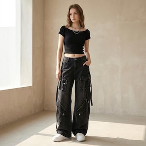Peut inclure: Un haut court noir à manches courtes avec une encolure large, associé à un pantalon cargo en jean noir ample. Le pantalon présente de multiples poches utilitaires, des détails argentés, de longues lanières et des fermetures éclair diagonales.
