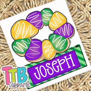 May include: A white t-shirt featuring a colorful illustration of a king cake with purple, green, and yellow icing. The name "JOSEPH" is displayed on a purple banner with a green and white striped background. The TTB Apparel logo is in the lower left corner.