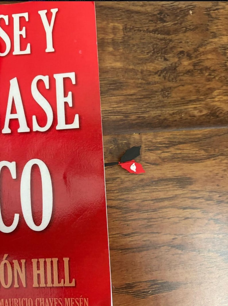 May include: A red book with white text and a decorative bookmark. The bookmark has a black and red design with a white heart shape. The book's cover is red with white text.