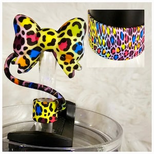 以下が含まれることがあります： カラフルなヒョウ柄のリボン型のボトルストッパーと、お揃いのバンド。リボンは黄色、ピンク、青、オレンジの斑点模様です。バンドは黒いタンブラーに巻かれています。目を引くデザインです。