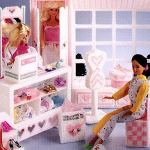 Pode incluir: Um padrão de loja boutique de bonecas de moda em tela plástica. O conjunto inclui uma boutique com janela, cabides, prateleiras, cadeiras e acessórios. O esquema de cores é principalmente rosa e branco, com bonecas e roupas expostas.