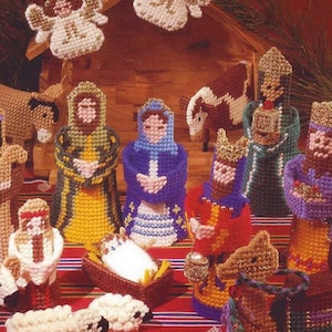 Puede incluir: Un juego de Natividad de lona de plástico con figuras de ángeles, María, José, el niño Jesús, los tres reyes magos, ovejas y un burro. Las figuras están hechas con hilo y están sobre un fondo a rayas rojas y blancas.