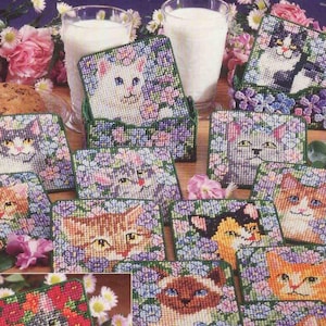 May include: A dozen plastic canvas kitty coaster set with twelve designs, plus two caddies. Each coaster features a different cat face surrounded by floral patterns. The coasters are displayed with milk glasses and cookies.