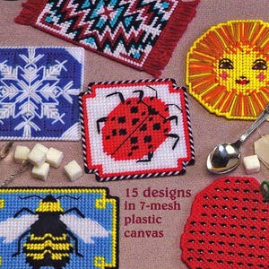 May include: A collection of colorful, handmade plastic canvas mug rugs with various designs, including a snowflake, ladybug, bee, and a strawberry. The text "Mighty MugRugs" and "15 designs in 7-mesh plastic canvas" are visible.