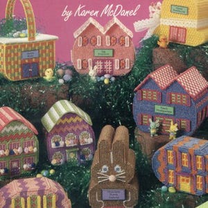 May include: A collection of colorful plastic canvas Easter egg village designs. The designs include houses, a basket, and a bunny, all crafted with needlework. The text on the cover reads "Easter Egg Village" and "plastic canvas".