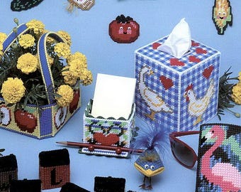 May include: A collection of plastic canvas crafts, including a basket of flowers, tissue box, and small lettered boxes. The image features various food-shaped and animal-shaped needlepoint designs, with the text "plastic canvas BAZAAR" at the top.