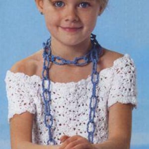 May include: A white, off-the-shoulder crochet top with short sleeves. A blue beaded necklace is draped around the neck and chest. The person is wearing blue shorts. The background is a light blue.