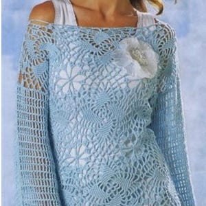 May include: A light blue crochet top with a delicate floral pattern. The top has a wide, open neckline and long sleeves. A white flower brooch is pinned to the front of the top.