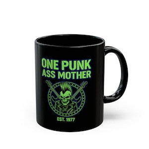 May include: Black ceramic mug featuring the text "ONE PUNK ASS MOTHER" in green, above a skull with a mohawk and crossed guitars. The text "EST. 1977" is below the graphic.