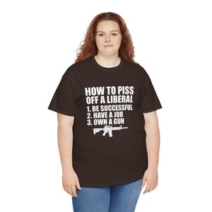 May include: A dark brown short-sleeved t-shirt featuring white text that reads: HOW TO PISS OFF A LIBERAL 1. BE SUCCESSFUL 2. HAVE A JOB 3. OWN A GUN, accompanied by a white graphic illustration of a rifle positioned below the text.