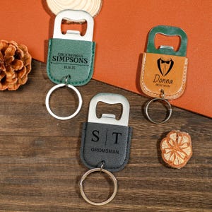 May include: Three leather bottle opener keychains with different designs. One is green with the text "Groomsman Simpsons 10.10.25", one is brown with the text "Donna Best Man" and a tuxedo graphic, and one is black with the text "S|T Groomsman".