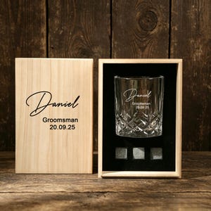 Può includere: Un bicchiere da whisky in cristallo trasparente con motivo a diamante e il testo inciso "Daniel Groomsman 20.09.25" in una scatola di legno con rivestimento in velluto nero, con tre pietre da whisky grigie e un coperchio in legno abbinato.