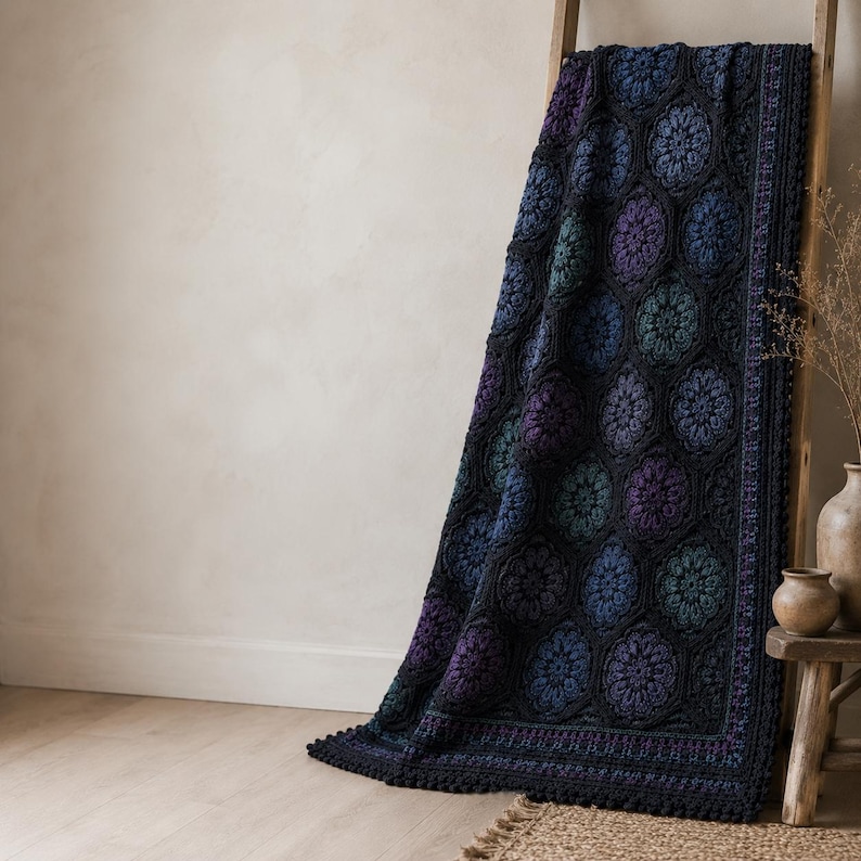 May include: A crochet blanket featuring a repeating pattern of hexagonal motifs in shades of deep blue, purple, and teal, framed by a black border. The blanket has a textured surface with intricate floral-like designs and a scalloped edge finish.
