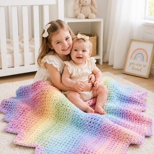 Könnte beinhalten: Eine handgefertigte Häkeldecke für Babys mit einem lebendigen Regenbogen-Farbverlauf und einem strukturierten, gewellten Rand. Die Decke zeigt einen weichen Farbübergang von Violett und Blau zu Grün, Gelb, Orange und Rosa in dicker Maschenoptik.