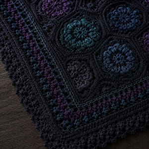 May include: A dark-toned crochet blanket featuring a repeating pattern of hexagonal motifs with intricate floral centers in shades of deep blue, teal, and purple. The edges are finished with a textured, scalloped border in a solid dark charcoal.
