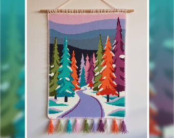 Op de afbeelding: Een kleurrijke, handgemaakte wandhanger met een winterlandschap. De wandtapijt toont een besneeuwd pad dat door een bos van levendige bomen in groen, oranje, paars en teal slingert. Bevestigd aan een houten stok aan de bovenkant, met decoratieve kwasten.
