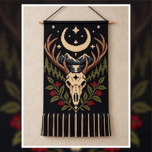May include: A rectangular wall hanging featuring a cross-stitch design on a black background. The image depicts a deer skull with large antlers, a crescent moon, stars, mountain peaks, pine trees, and green foliage with red berries.