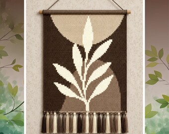 May include: A rectangular wall hanging featuring a crocheted leaf pattern in cream against a dark brown and tan background. The piece is suspended from a wooden dowel with a cord and finished with a row of alternating cream and brown tassels.