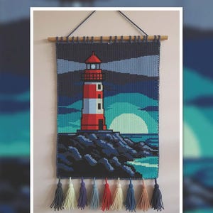 Peut inclure: Tapisserie murale au crochet repr&eacute;sentant un phare au coucher du soleil. Le motif comprend un phare rouge et blanc, un oc&eacute;an bleu et un soleil jaune. La tapisserie mesure 100x150 cm et est orn&eacute;e de pompons color&eacute;s.