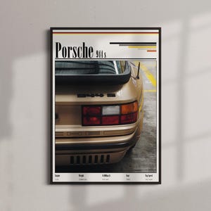 Puede incluir: Póster enmarcado con un Porsche 911s dorado. La imagen muestra la parte trasera del coche con el nombre del modelo y un alerón negro. El póster tiene un marco negro y se muestra contra una pared gris claro.