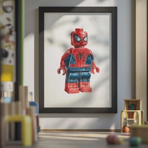 May include: Framed artwork featuring a Lego-style Spider-Man figure. The figure is predominantly red and blue, with a detailed design. The artwork is displayed in a black frame, adding a classic touch to the superhero theme.